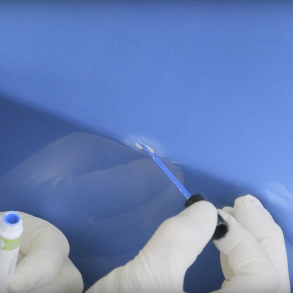 A person utilizing a small brush to perform touch-up painting on a car, the paint being applied is a shade of light blue