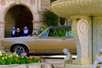 Three nuns walk out to a dormitory while a 1967 Pontiac LeMans is parked outside.