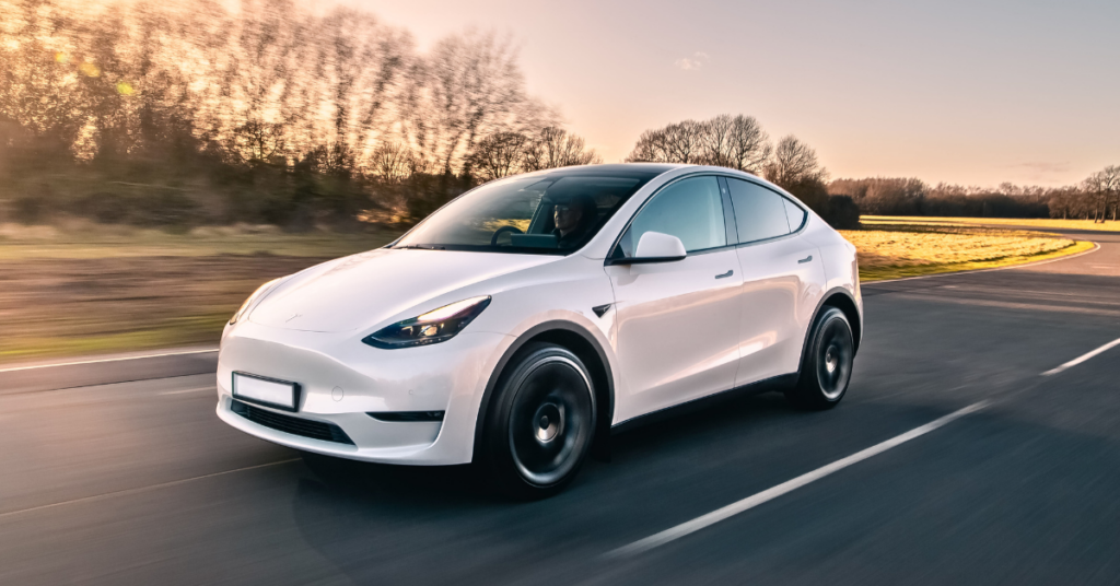 A white Tesla Model Y driving down a road.