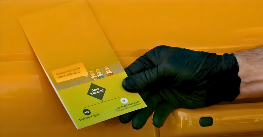 A gloved hand compares a perfectly matched orange test card against the surface of an orange car. 