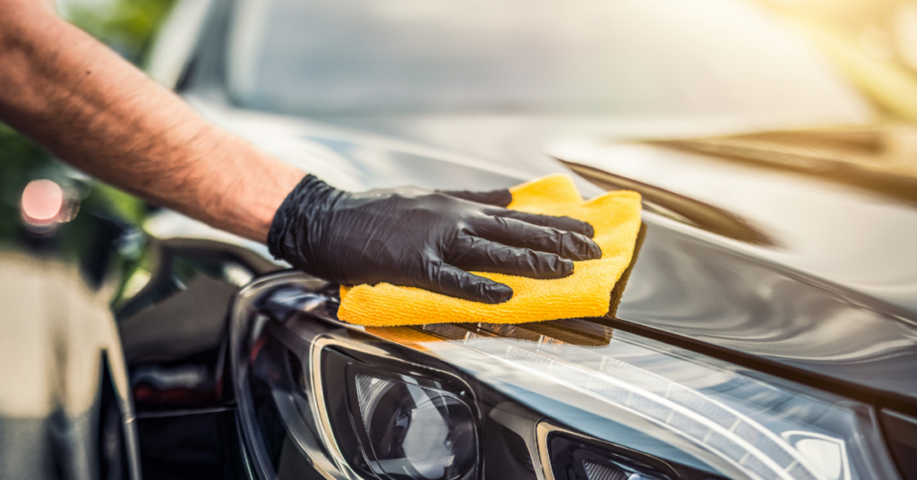 A gloved hand wipes down a black car. 