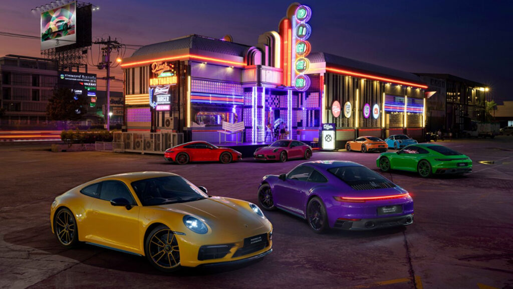 Porsches in Signal Yellow, Ultraviolet, Signal Green, Fire Red, Ruby Star, Pastel Orange, & Riviera Blue are parked in front of a Thai diner that is lit up in neon.