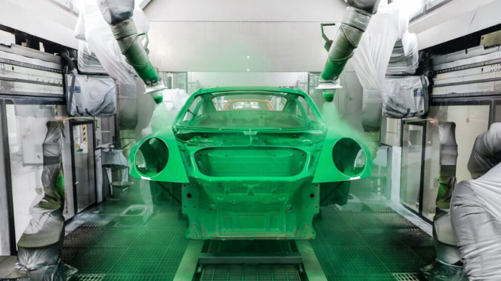 Two large hoses spray the unfinished body of a car with Essmann Green Paint.