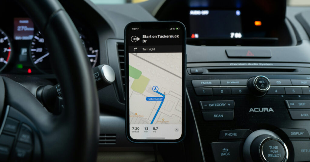 A phone attached to the dashboard of a car shows a satellite navigation app. A route is planned out on the map.