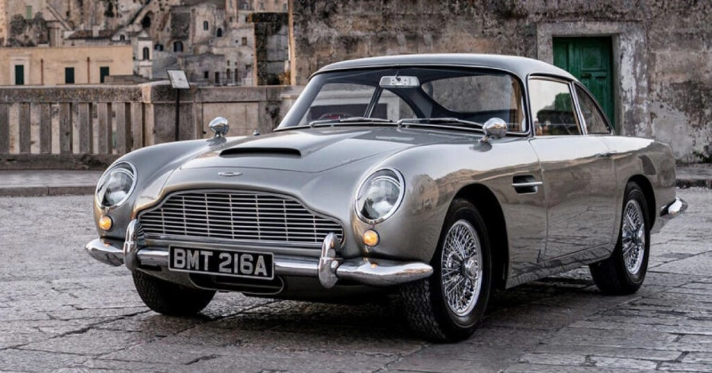 A silver 1964 Aston Martin DB5 parked on a stone road.
