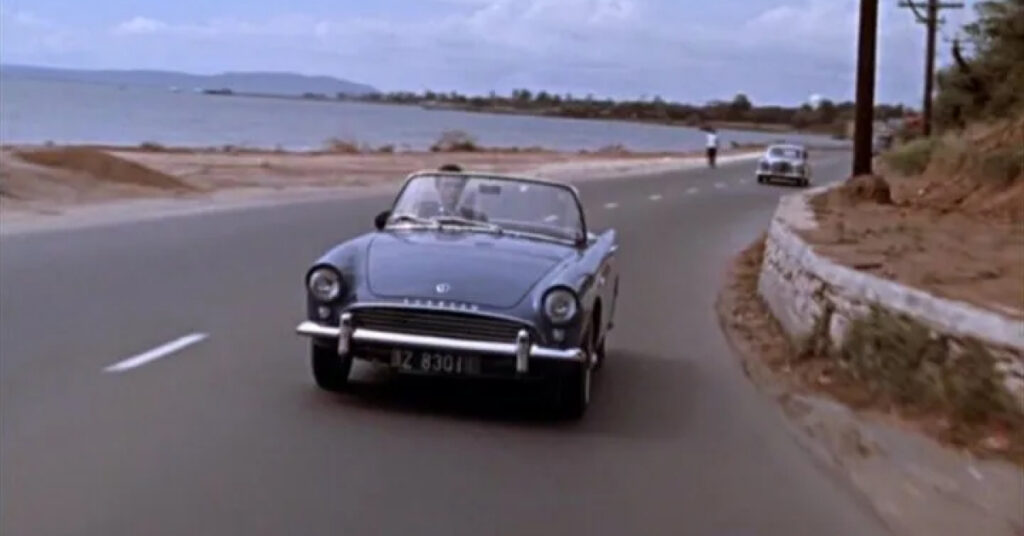James Bond drives a blue 1961 Sunbeam Alpine Series II down a road.