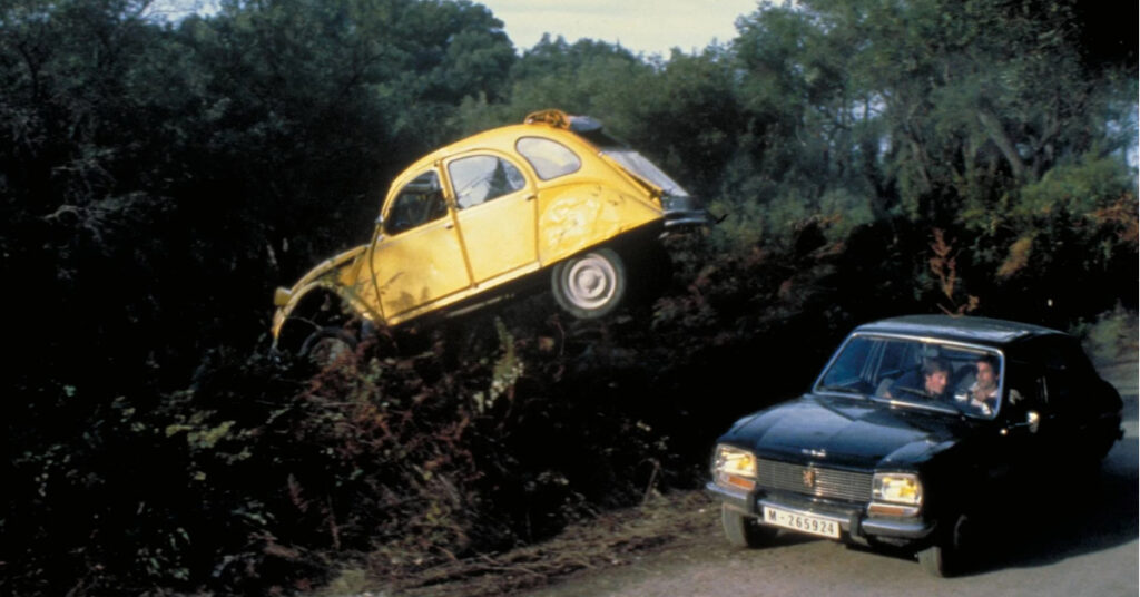 A yellow Citroën 2CV flies through the air as it is chased by henchmen in a black Peugeot 504.